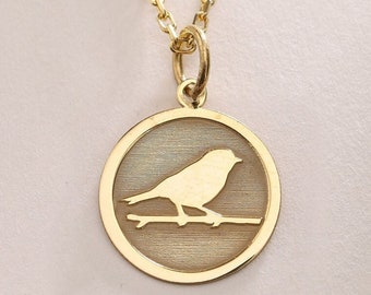 Könnte beinhalten: Eine goldene Halskette mit einem runden Anhänger, der die Silhouette eines Vogels auf einem Ast zeigt.