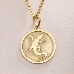 May include: A gold chain necklace with a round pendant featuring a cutout silhouette of a lizard.