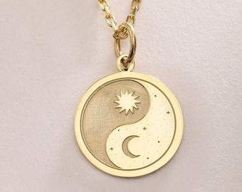 May include: A gold necklace with a round pendant featuring a yin yang symbol with a sun and moon design.