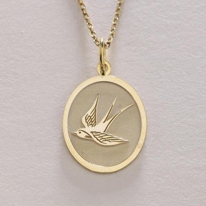 Peut inclure: Un collier en chaîne dorée avec un pendentif représentant une hirondelle en vol gravée avec délicatesse. Le pendentif est de forme ovale et présente une finition lisse et polie.