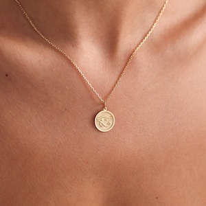 Op de afbeelding: Een gouden ketting met een ronde hanger met een gegraveerd oog van Horus-symbool.