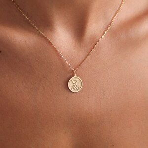 May include: A gold chain necklace with a round pendant featuring a stylised symbol. The pendant is approximately 2.5 cm in diameter.