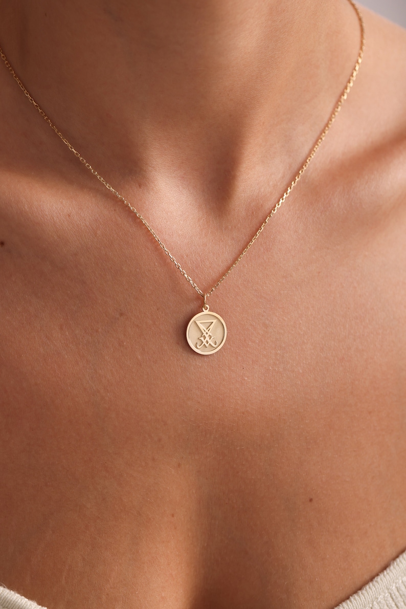 May include: A gold chain necklace with a round pendant featuring a stylised symbol. The pendant is approximately 2.5 cm in diameter.