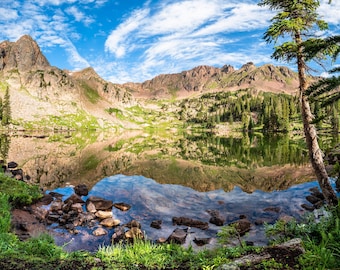 May include: A mountain lake surrounded by lush green trees and rocky mountains. The water is still and reflects the sky and mountains.