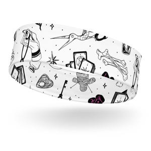 Puede incluir: Diadema blanca con un diseño oculto en negro y rosa. El diseño incluye ilustraciones de cartas del tarot, huesos, una muñeca vudú y otros símbolos místicos. Un accesorio cómodo para el uso diario.