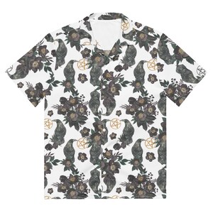 May include: A white short-sleeved button-up shirt with a repeating pattern of black ravens, dark flowers, and gold pentagrams.