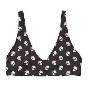 Könnte beinhalten: Schwarzes Bikini-Oberteil mit einem sich wiederholenden Muster aus Alien-Gesichtern in Pastellrosa und -blau. Das Oberteil hat einen U-Ausschnitt und breite Träger.