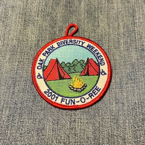 May include: A circular patch with a red border and a loop at the top. The patch features a camping scene with two red tents, a campfire, and the text "OAK PARK DIVERSITY WEEKEND 2001 FUN-O-REE".