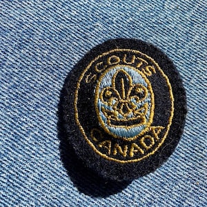May include: A black and gold embroidered Scouts Canada patch with a fleur-de-lis design.