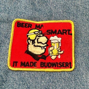 May include: Red embroidered patch with a yellow border. It features a cartoon man holding a glass of beer and the text "Beer Makes Smart It Made Budweiser!"