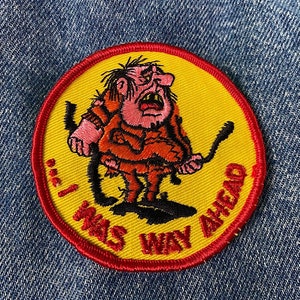 May include: A yellow and red embroidered patch featuring a cartoon character holding a stick. The text on the patch reads "I Was Way Ahead".