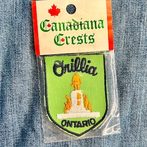 May include: A green and white embroidered patch with the text "Orillia" and "ONTARIO" in black. The patch is packaged in a clear plastic bag with a white card that reads "Canadiana Crests" with a Canadian maple leaf logo.