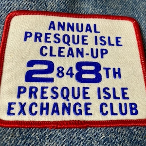 May include: White patch with red stitching around the edges. The patch says "Annual Presque Isle Clean-Up 284th Presque Isle Exchange Club" in blue lettering.