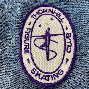 May include: Oval patch with a white center and a purple border. The patch reads "THORNHILL FIGURE SKATING CLUB" in purple text. A purple figure skater is in the center. Two small stars are above the skater.