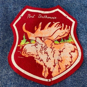 May include: Red felt patch with a white border, featuring a cartoon moose with large antlers and the text "Port Dalhousie" in white cursive.