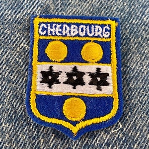 May include: A blue and yellow embroidered patch with the text "CHERBOURG" in white. The patch features three white stars with black centers and three yellow circles.