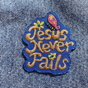 May include: A blue embroidered patch with the text "Jesus Never Fails" in gold thread. The patch features a pink butterfly with yellow flowers.