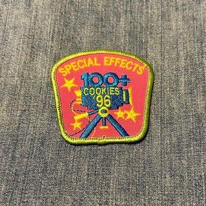 May include: An embroidered patch in pink and yellow, featuring the text "SPECIAL EFFECTS", "100+ COOKIES '96", a blue film camera on a tripod, and yellow star details. The patch has a green border.