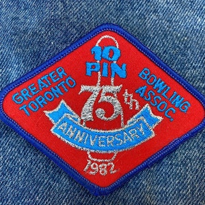 May include: A red diamond-shaped patch with blue trim. It says "Greater Toronto Bowling Assoc." and "10 Pin 75th Anniversary 1982" in white lettering.