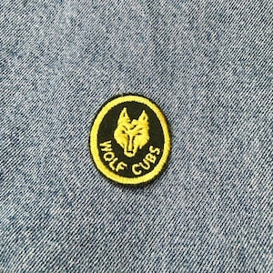 May include: A black and yellow embroidered patch with a wolf head design and the text "Wolf Cubs".