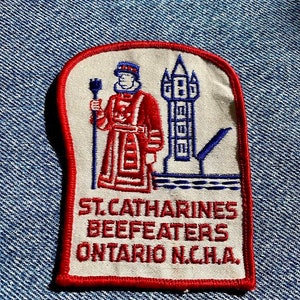 May include: A red, white, and blue embroidered patch with a cartoon image of a person in a red and white uniform holding a staff. The text on the patch reads "St. Catharines Beefeaters Ontario N.C.H.A."