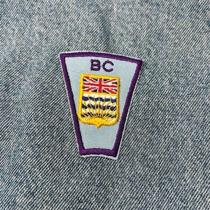 May include: An embroidered patch in blue and purple with the text "BC" and the coat of arms of British Columbia.