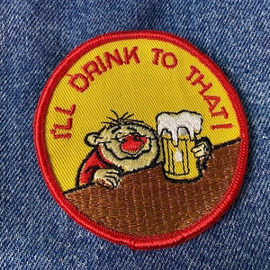 May include: A red, white and yellow embroidered patch featuring a cartoon character holding a glass of beer. The text on the patch reads "I'll drink to that!"