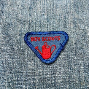 May include: Blue and red embroidered patch with the text "BOY SCOUTS" and a red watering can design.