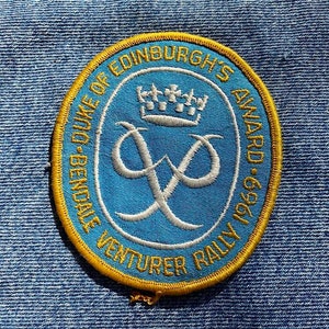 May include: A blue and gold embroidered patch with the text "The Duke of Edinburgh's Award - 1969 Venturer Rally" and a crown and the letter "X" in white.