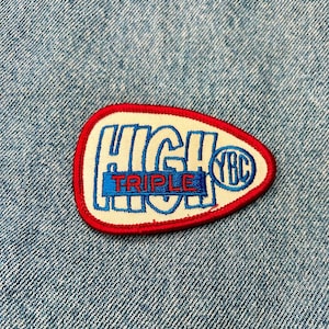 May include: A white and red embroidered patch with the text "HIGH" in blue and "TRIPLE" in red. The patch has a white background and a red outline.