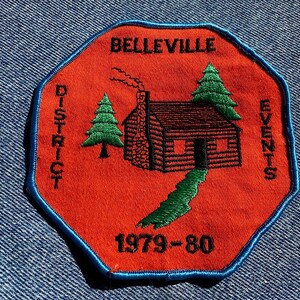 May include: A red octagonal patch with blue edging, featuring a cabin with a chimney, two green trees, and the text "Belleville District Events 1979-80".