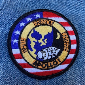 Peut inclure: Écusson brodé représentant l'insigne de la mission Apollo 1. L'écusson circulaire a une bordure bleue avec des étoiles blanches et des rayures rouges et blanches. Le centre montre un globe, une fusée et les noms "GRISSOM", "WHITE" et "CHAFFEE".