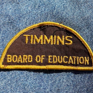 May include: A brown and gold embroidered patch with the text "TIMMINS BOARD OF EDUCATION".