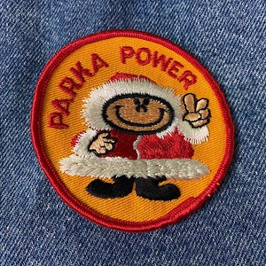 May include: A yellow and red embroidered patch with a cartoon character wearing a red and white Santa hat and a red coat. The text "PARKA POWER" is written around the character.