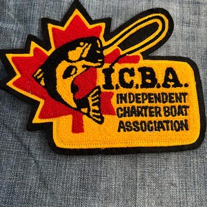May include: A yellow and black embroidered patch with a fish jumping out of a red maple leaf. The text "ICBA. INDEPENDENT CHARTER BOAT ASSOCIATION" is on the patch.