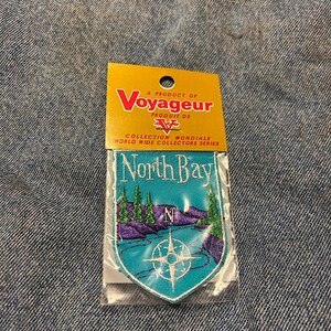 May include: A Voyager patch with a teal and purple landscape design and the words "North Bay." The patch includes a compass rose and is part of the World Wide Collectors Series.