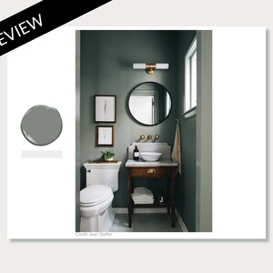 K&ouml;nnte beinhalten: Ein kleines Badezimmer mit einer dunkelgr&uuml;nen Wand, einer wei&szlig;en Porzellan-Toilette, einem wei&szlig;en Porzellan-Waschbecken, einem Holzwaschtisch mit goldenem Schubladenknauf, einem runden Spiegel mit schwarzem Rahmen und einer goldenen Leuchte.