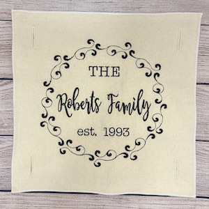 Puede incluir: Una pared de lona beige con bordado negro. El bordado presenta un diseño de desplazamiento decorativo con el texto "THE Roberts Family est. 1993".