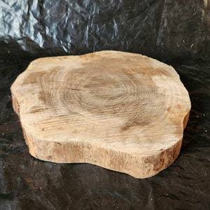 May include: A natural wood slice with a light brown color and a rough, irregular edge. The wood has a circular grain pattern and is perfect for crafting or decorating.