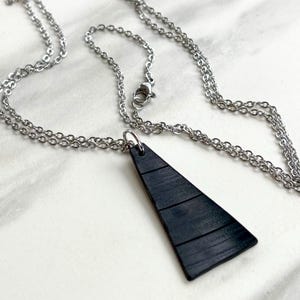 May include: A silver chain necklace with a black triangular pendant. The pendant has a textured, layered design.