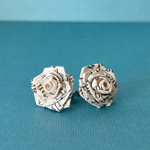 Handmade paper rose earrings made from book paper sitting on a blue background.