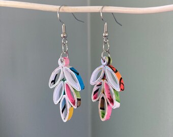 May include: A pair of leaf-shaped earrings with white paper outlines and colorful paper inserts. The earrings have silver-colored fish hook ear wires. The paper inserts feature pink, blue, green, and yellow hues.