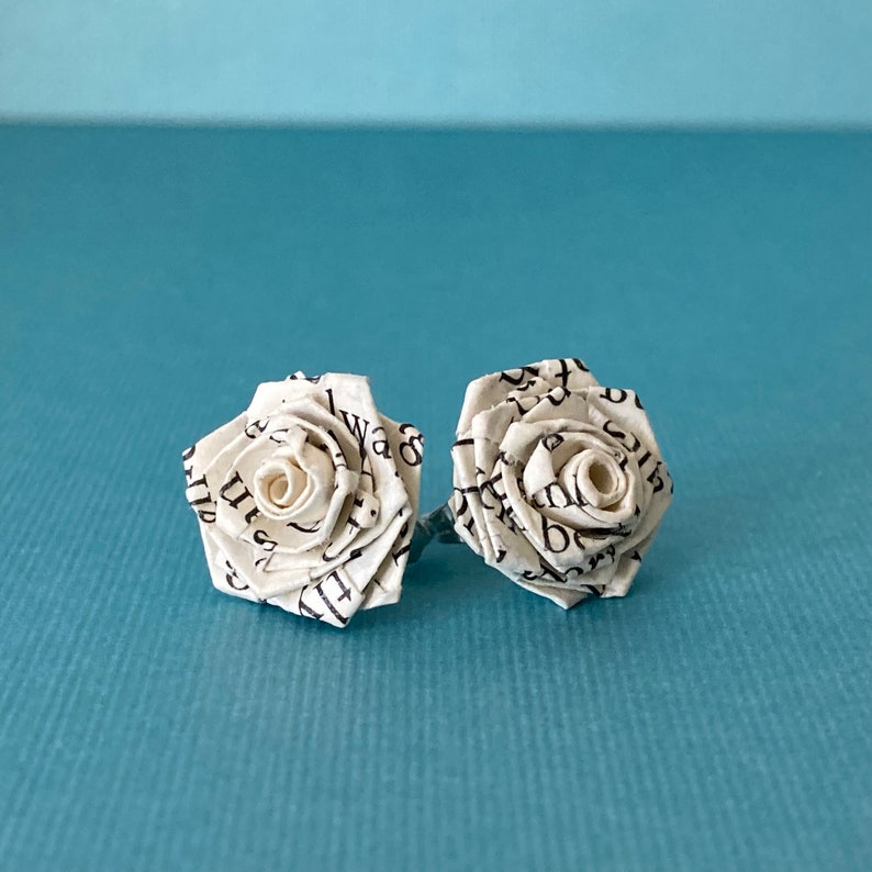 Handmade paper rose earrings made from book paper sitting on a blue background.