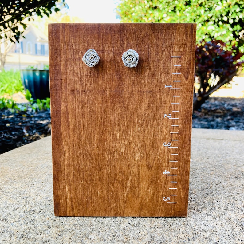 Handmade paper rose earrings made from book paper being measured on a wood measuring box.