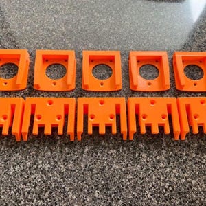 May include: Ten orange plastic brackets are arranged in two rows. The top row has five brackets with a circular hole in the center. The bottom row has five brackets with a series of vertical slots.
