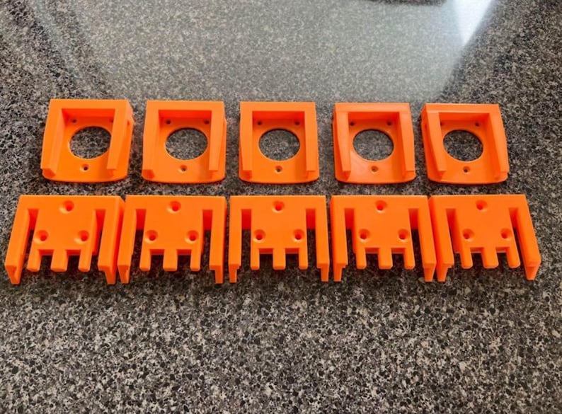 May include: Ten orange plastic brackets are arranged in two rows. The top row has five brackets with a circular hole in the center. The bottom row has five brackets with a series of vertical slots.