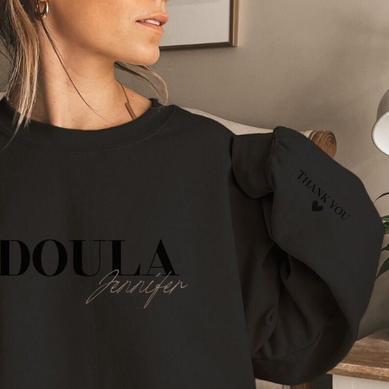 Sweatshirt for a doula, with doula printed on the front with her name below it. On the sleeve, there is a thank you print with a hart