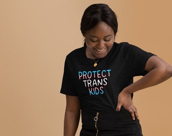 May include: A person wearing a black t-shirt with the text "PROTECT TRANS KIDS" in rainbow colors and a black skirt.