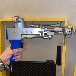 Può includere: Uno strumento elettrico blu e argento con un manico nero e un cavo giallo. Lo strumento ha una spazzola e una serie di bracci metallici. Lo strumento è tenuto nella mano di una persona.