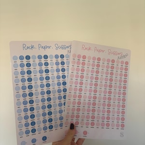 Puede incluir: Dos hojas rectangulares con el tema de Piedra, Papel, Tijeras. Una hoja presenta círculos azules, la otra rosas. Cada círculo contiene las palabras "Piedra", "Papel" o "Tijeras". El texto "Piedra. Papel. Tijeras" está en la parte superior.